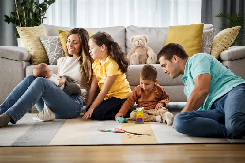 Família brincando no chão da sala, com o bebê no colo da mãe